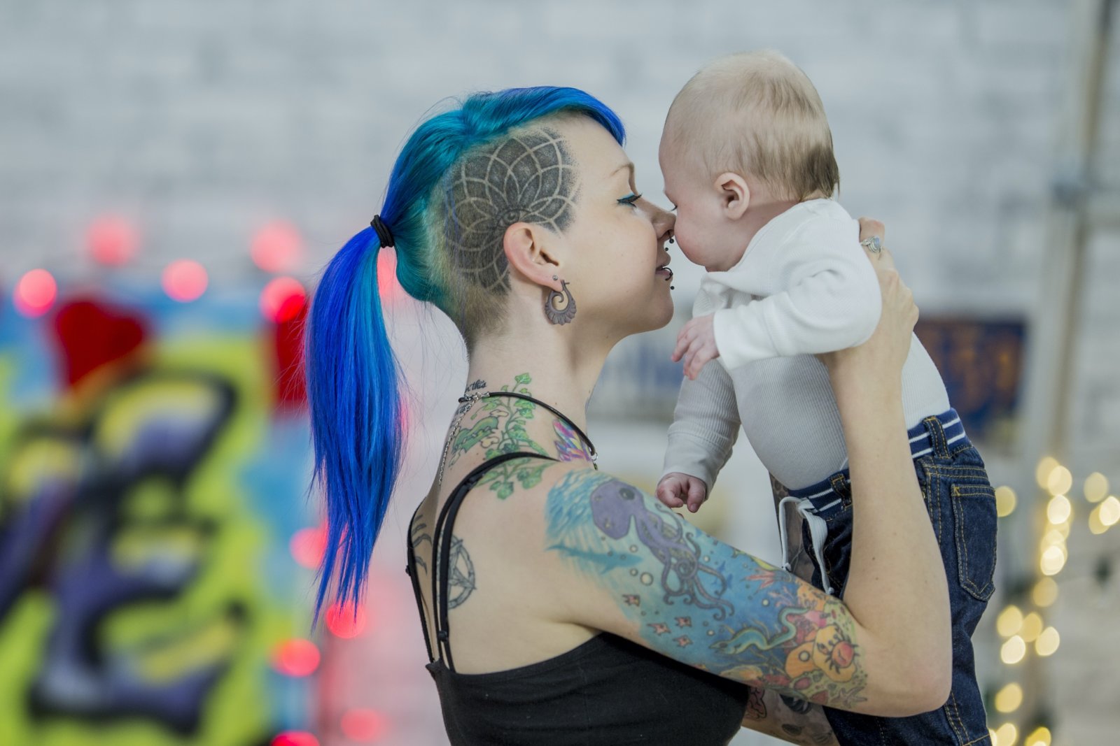 a heavily tattooed girl tenderly holding an infant